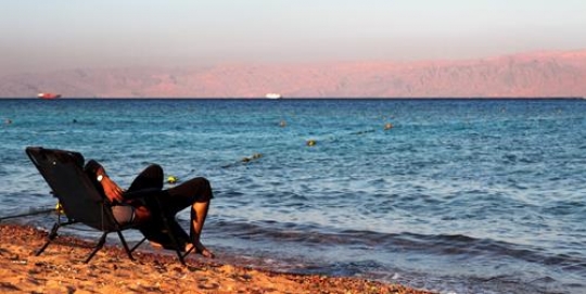 man sitting in sandy beach,aqaba