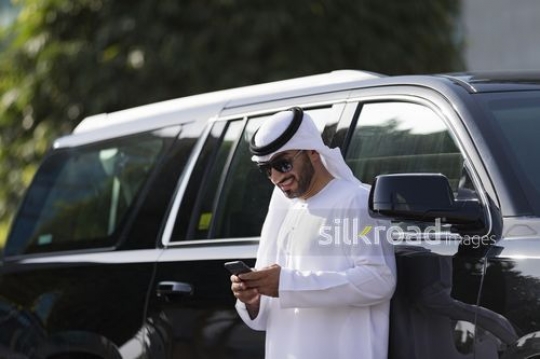 Arab businessman standing next to the car using his mobile|-