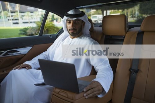Middle Eastern Businessman sitting inside the luxury car using his laptop|