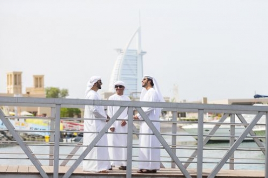 Men dressed in the traditional UAE attire standing by the dock talking to each other|