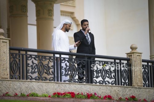Business man on his phone standing next to his colleague drinking from his travel mug|-