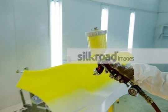 Mechanic spray painting a part of the car yellow|