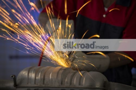 Worker using the machine to cut the metal part for the car|