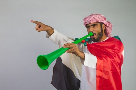 Arab man screaming in the horn wearing the UAE flag on his back