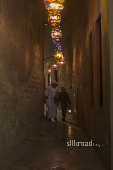 Middle Eastern father and son walking through the pathway decorated by Ramadan Lanterns|-