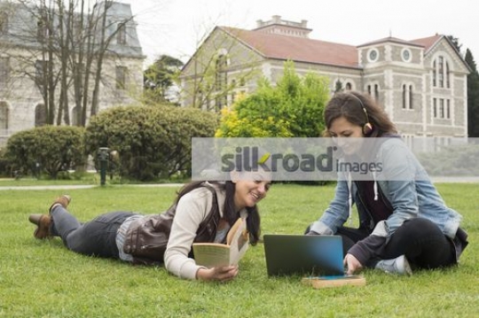 Two girls sitting on the grass talking|