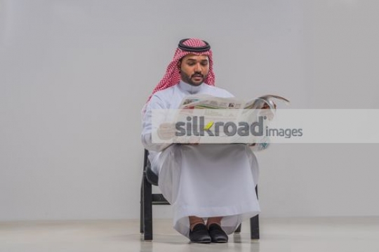 Arab man sitting on the chair reading the newspaper