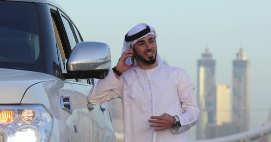 Arab Businessman standing outside his car talking on the phone|-
