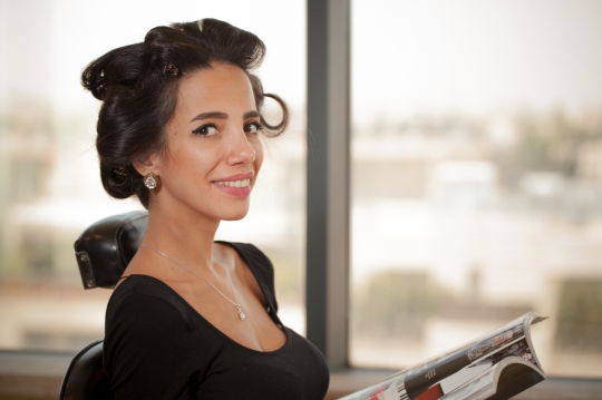 Middle Eastern woman sitting down at the hair salon reading a magazine|