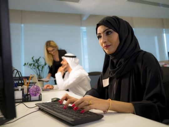 Business woman sitting by her desk with a background of business people working together|