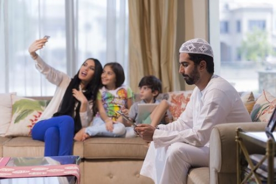 Arab father on his device while the mother and the kids are taking a picture|-