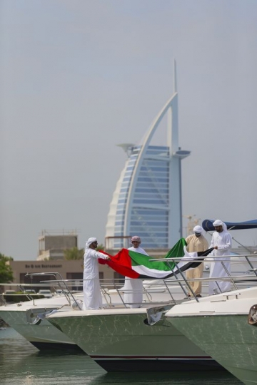 Arab men holding a UAE flag together on a yacht to celebrate National Day|