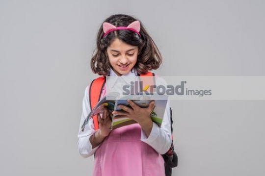 Young girl reading the book carrying her school bag|